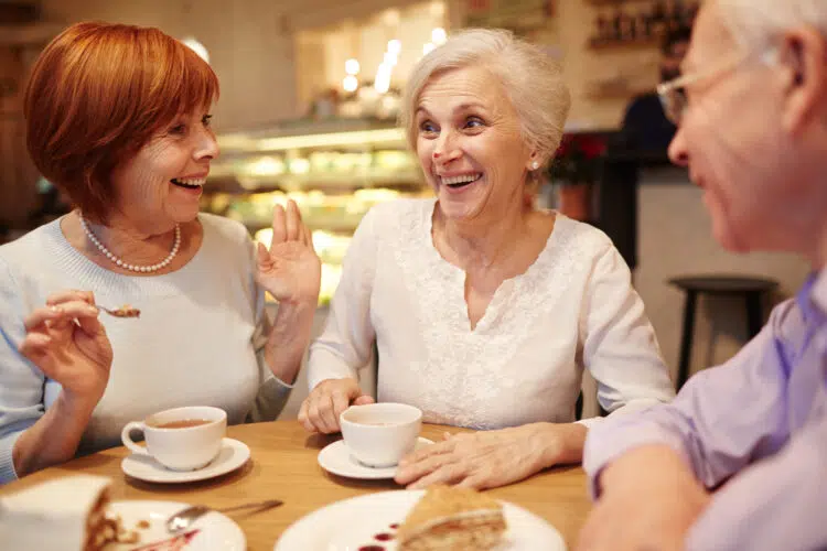 Three elderly people enjoying tea and cake together.