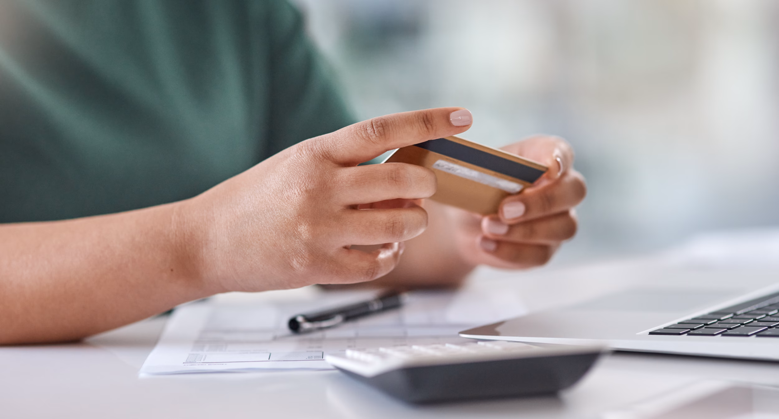 Person holding mobile phone over desk with calculator and financial documents, managing payroll payments.