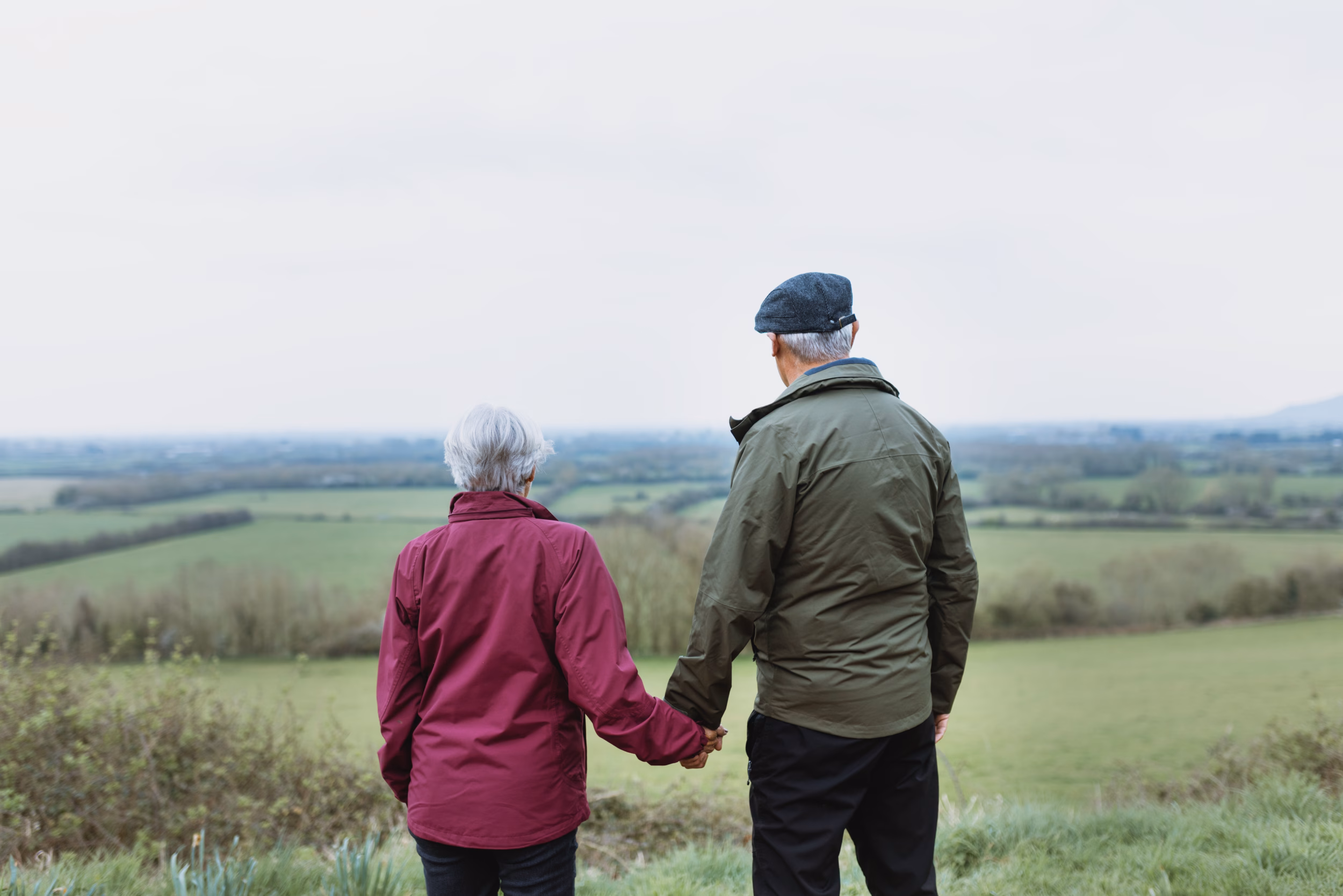 Elderly Couple, Outdoor Scene, Holding Hands. Elderly Couple Enjoying Nature, Wearing Jackets. Scenic View With Elderly Couple In A Peaceful Setting. Happy Couple Enjoy Nature. Happy Retirement