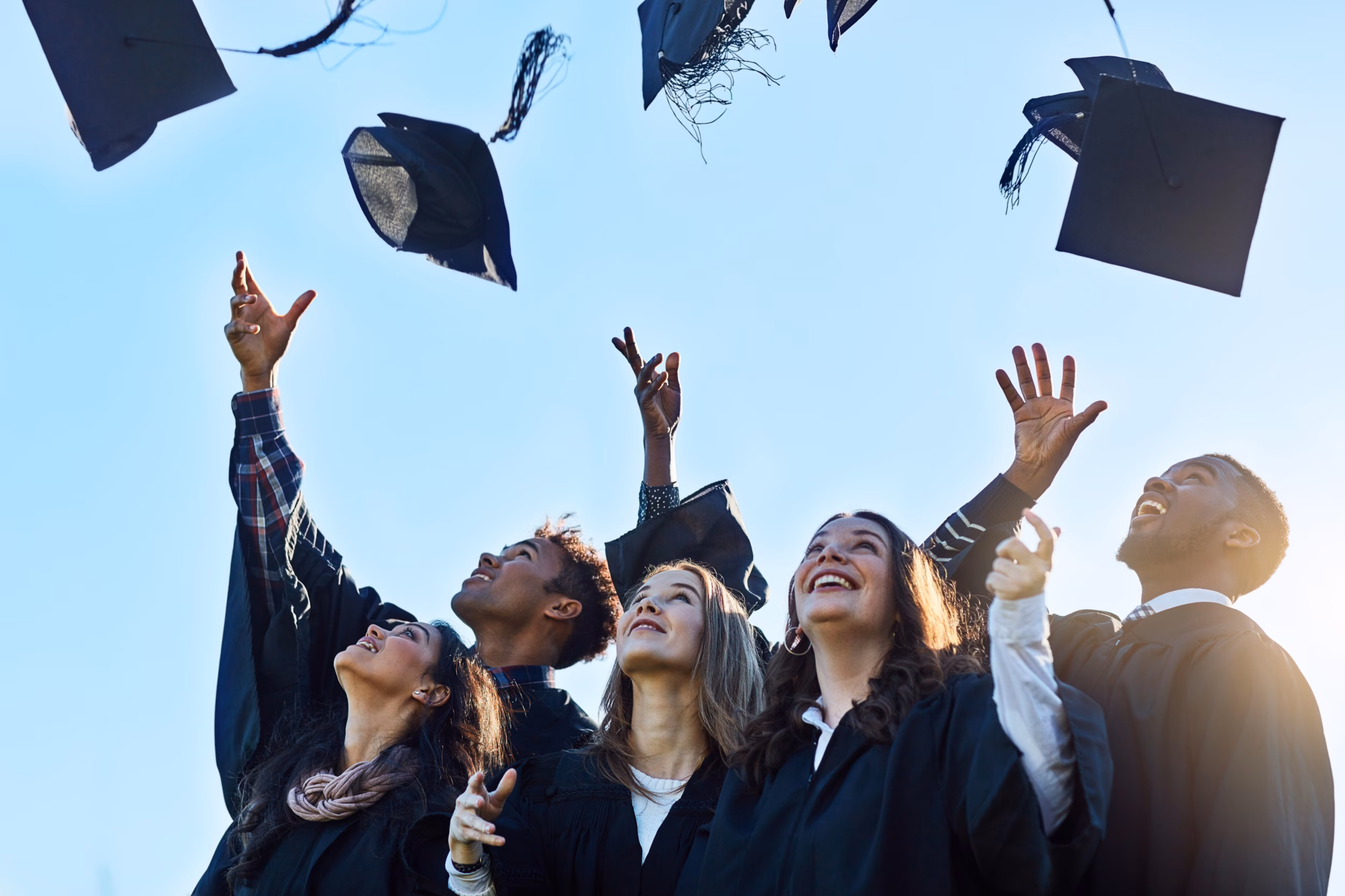 University Graduates Throwing Mortarboard Caps Into The Air In Celebration.