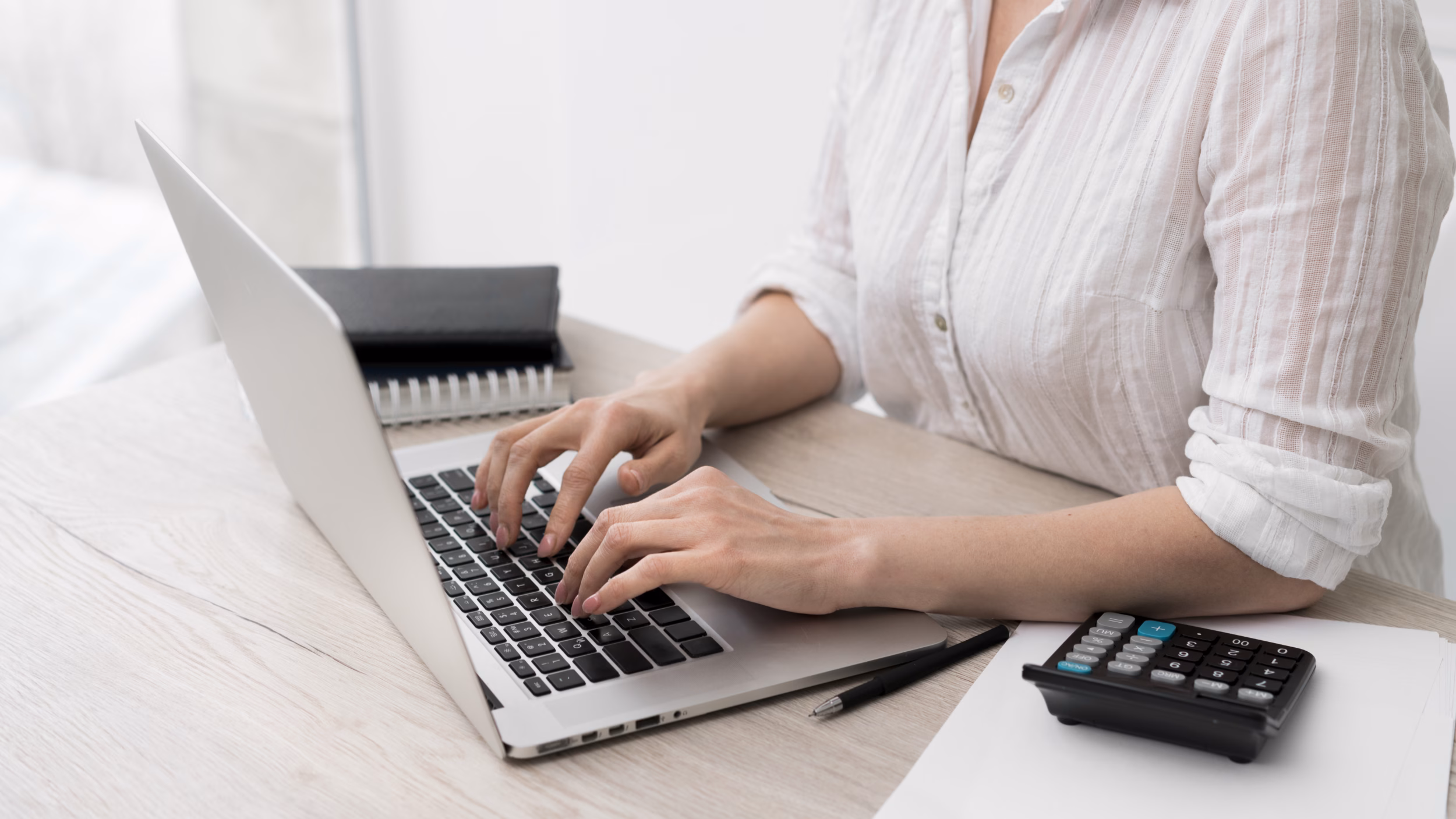 Person typing on a laptop with a calculator on the desk