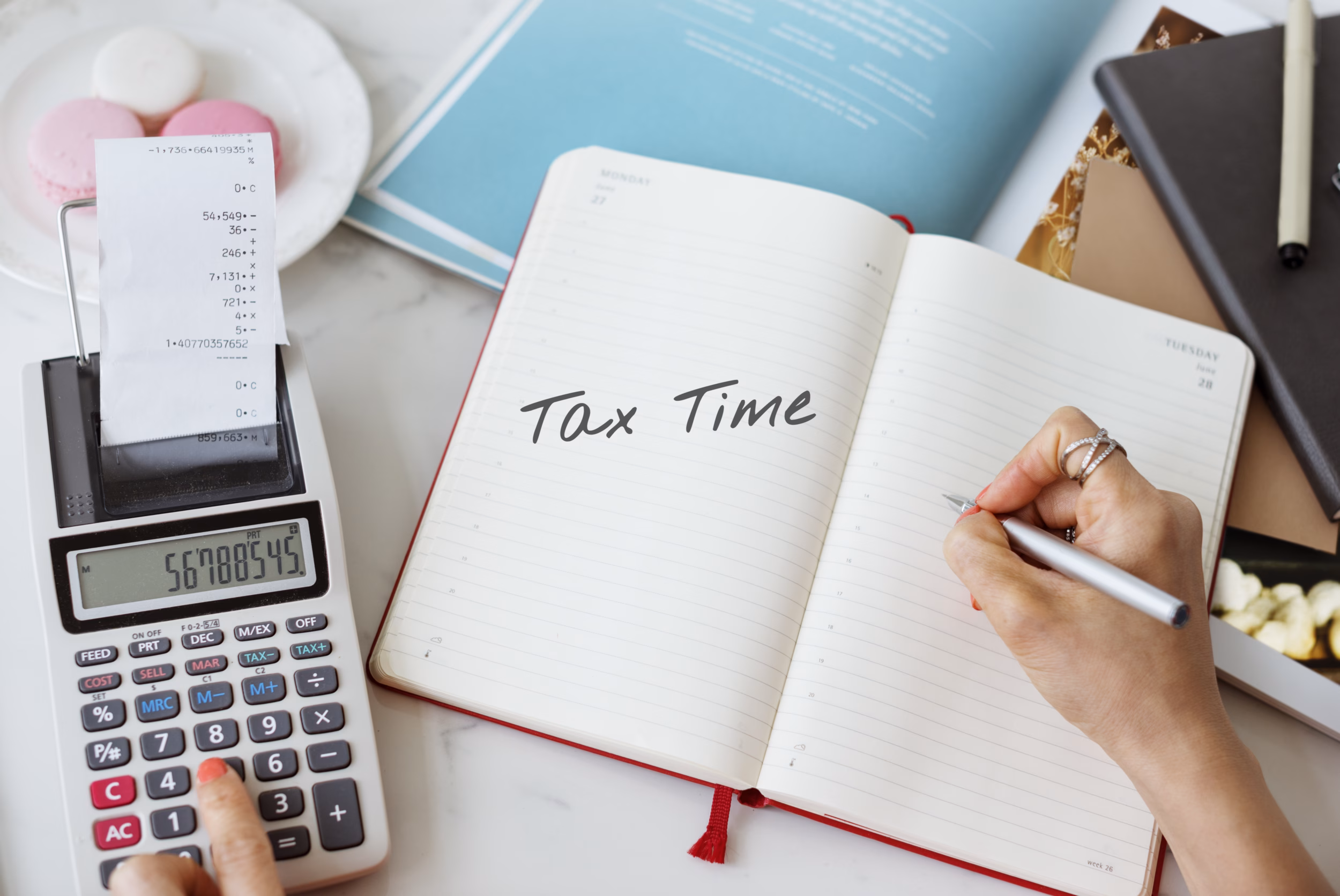 Person writing tax time in a notebook next to a calculator