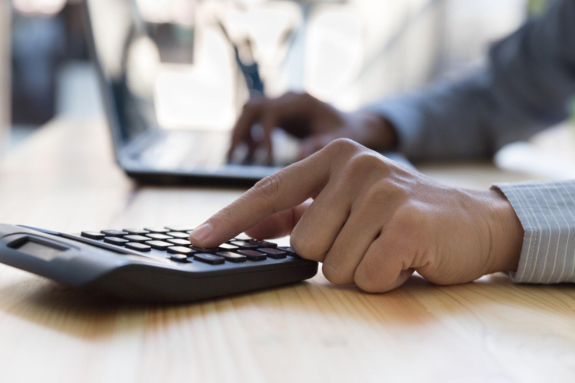 Person using a calculator and laptop at a desk